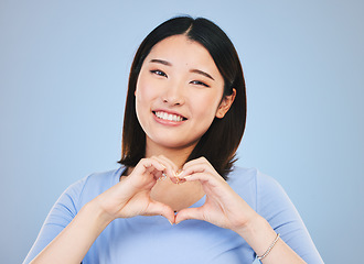 Image showing Happy asian woman, portrait and heart hands, love sign or gesture in romance against a blue studio background. Female person smile in happiness with loving emoji, shape or symbol for valentines day