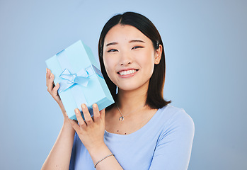 Image showing Happy, Asian woman and portrait with a gift, box and present on blue background in studio with promotion or discount. Model, smile and face with happiness for giving or receiving surprise package