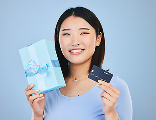 Image showing Woman, credit card and gift box, prize or retail giveaway and payment in portrait and a blue background. Happy Asian person or winner for present, finance bonus and shopping sale or success in studio