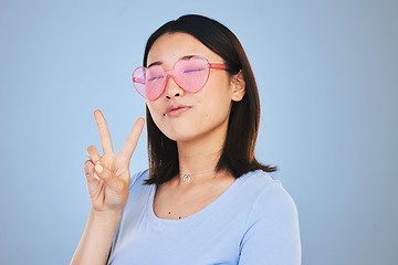 Image showing Peace, sign and portrait of woman with hand for emoji in studio blue background with gen z style, fashion or heart glasses. Face, pose and Asian model with cool gesture and expression on social media