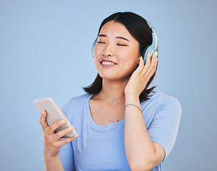 Image showing Music, headphones and happy Asian woman with phone for streaming radio, subscription and relax. Sound, online podcast and face of person listening to song, audio and track for calm on blue background