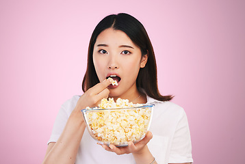 Image showing Popcorn, hungry and woman portrait eating a movie snack in a studio with watching tv and food. Pink background, Asian female person and surprise with chips in a glass bowl with film and series