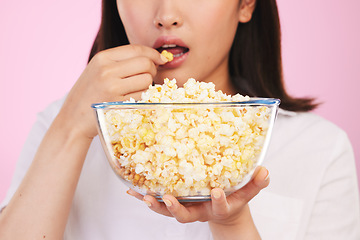 Image showing Popcorn, hungry and woman hands eating a movie snack in a studio with watching tv and food. Pink background, female person and mouth with chips in a glass bowl with film and series subscription