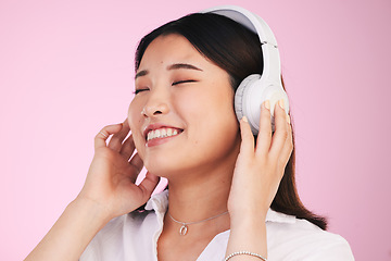 Image showing Headphones, happy and young woman in a studio listening to music, playlist or album for entertainment. Smile, calm and Asian female model streaming a song or radio isolated by a pink background.