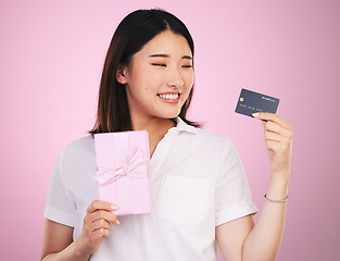 Image showing Credit card, gift box and young woman in a studio online shopping a sale, discount or deal. Happy, smile and Asian female model buying a present with retail promotion isolated by a pink background.