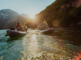 Image showing A group of friends enjoying fun and kayaking exploring the calm river, surrounding forest and large natural river canyons during an idyllic sunset.