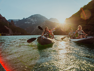 Image showing A group of friends enjoying fun and kayaking exploring the calm river, surrounding forest and large natural river canyons during an idyllic sunset.