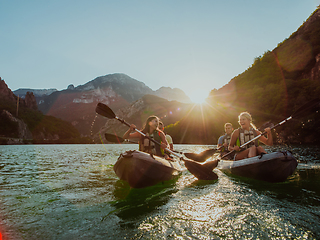 Image showing A group of friends enjoying fun and kayaking exploring the calm river, surrounding forest and large natural river canyons during an idyllic sunset.