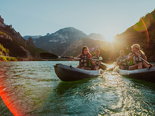 Image showing A group of friends enjoying fun and kayaking exploring the calm river, surrounding forest and large natural river canyons during an idyllic sunset.