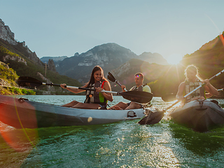 Image showing A group of friends enjoying fun and kayaking exploring the calm river, surrounding forest and large natural river canyons during an idyllic sunset.