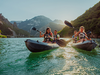 Image showing A group of friends enjoying fun and kayaking exploring the calm river, surrounding forest and large natural river canyons during an idyllic sunset.