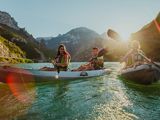 Image showing A group of friends enjoying fun and kayaking exploring the calm river, surrounding forest and large natural river canyons during an idyllic sunset.