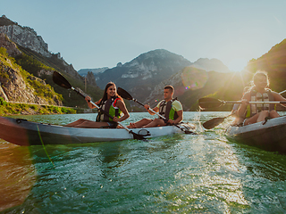 Image showing A group of friends enjoying fun and kayaking exploring the calm river, surrounding forest and large natural river canyons during an idyllic sunset.