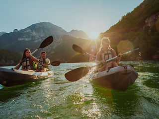 Image showing A group of friends enjoying fun and kayaking exploring the calm river, surrounding forest and large natural river canyons during an idyllic sunset.