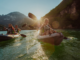 Image showing A group of friends enjoying fun and kayaking exploring the calm river, surrounding forest and large natural river canyons during an idyllic sunset.