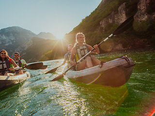 Image showing A group of friends enjoying fun and kayaking exploring the calm river, surrounding forest and large natural river canyons during an idyllic sunset.