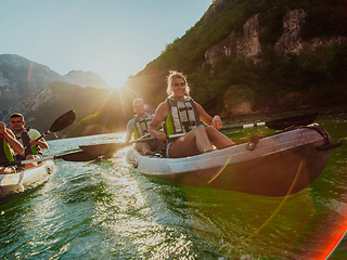 Image showing A group of friends enjoying fun and kayaking exploring the calm river, surrounding forest and large natural river canyons during an idyllic sunset.