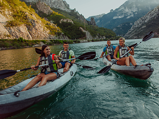 Image showing A group of friends enjoying fun and kayaking exploring the calm river, surrounding forest and large natural river canyons during an idyllic sunset.