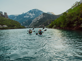 Image showing A group of friends enjoying fun and kayaking exploring the calm river, surrounding forest and large natural river canyons during an idyllic sunset.