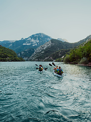 Image showing A group of friends enjoying fun and kayaking exploring the calm river, surrounding forest and large natural river canyons during an idyllic sunset.