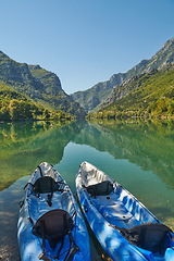 Image showing An idyllic photo of two kayaks on the river bank. In the background of green forest area and mountains