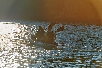 Image showing A young couple enjoying an idyllic kayak ride in the middle of a beautiful river surrounded by forest greenery in sunset time