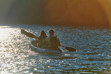 Image showing A young couple enjoying an idyllic kayak ride in the middle of a beautiful river surrounded by forest greenery in sunset time