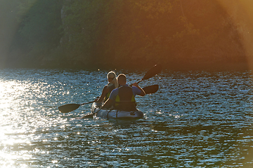 Image showing A young couple enjoying an idyllic kayak ride in the middle of a beautiful river surrounded by forest greenery in sunset time