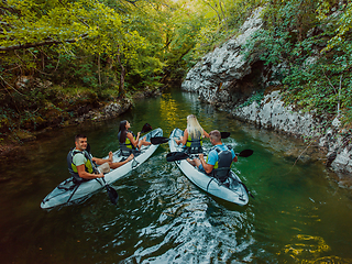 Image showing A group of friends enjoying having fun and kayaking while exploring the calm river, surrounding forest and large natural river canyons