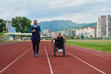 Image showing A Muslim woman in a burqa running together with a woman in a wheelchair on the marathon course, preparing for future competitions.