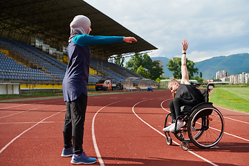 Image showing Two strong and inspiring women, one a Muslim wearing a burka and the other in a wheelchair stretching and preparing their bodies for a marathon race on the track