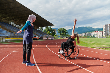 Image showing Two strong and inspiring women, one a Muslim wearing a burka and the other in a wheelchair stretching and preparing their bodies for a marathon race on the track