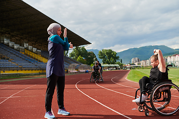 Image showing Two strong and inspiring women, one a Muslim wearing a burka and the other in a wheelchair stretching and preparing their bodies for a marathon race on the track