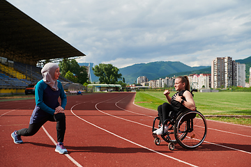 Image showing Two strong and inspiring women, one a Muslim wearing a burka and the other in a wheelchair stretching and preparing their bodies for a marathon race on the track