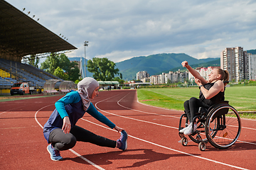 Image showing Two strong and inspiring women, one a Muslim wearing a burka and the other in a wheelchair stretching and preparing their bodies for a marathon race on the track