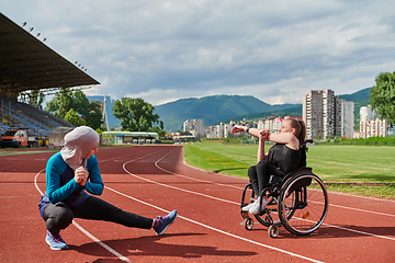 Image showing Two strong and inspiring women, one a Muslim wearing a burka and the other in a wheelchair stretching and preparing their bodies for a marathon race on the track