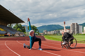 Image showing Two strong and inspiring women, one a Muslim wearing a burka and the other in a wheelchair stretching and preparing their bodies for a marathon race on the track