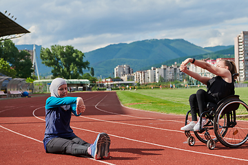 Image showing Two strong and inspiring women, one a Muslim wearing a burka and the other in a wheelchair stretching and preparing their bodies for a marathon race on the track