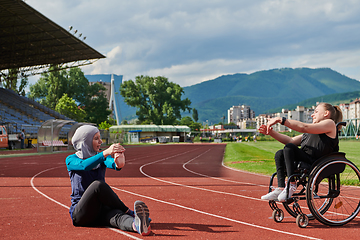 Image showing Two strong and inspiring women, one a Muslim wearing a burka and the other in a wheelchair stretching and preparing their bodies for a marathon race on the track