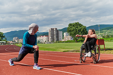 Image showing Two strong and inspiring women, one a Muslim wearing a burka and the other in a wheelchair stretching and preparing their bodies for a marathon race on the track