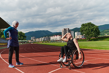 Image showing Two strong and inspiring women, one a Muslim wearing a burka and the other in a wheelchair stretching and preparing their bodies for a marathon race on the track