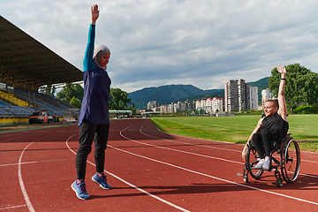 Image showing Two strong and inspiring women, one a Muslim wearing a burka and the other in a wheelchair stretching and preparing their bodies for a marathon race on the track