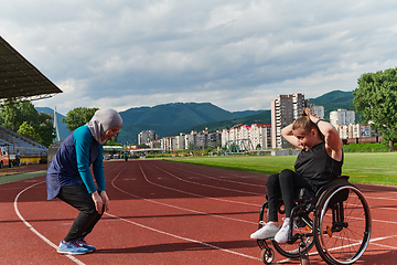 Image showing Two strong and inspiring women, one a Muslim wearing a burka and the other in a wheelchair stretching and preparing their bodies for a marathon race on the track