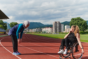 Image showing Two strong and inspiring women, one a Muslim wearing a burka and the other in a wheelchair stretching and preparing their bodies for a marathon race on the track