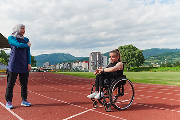 Image showing A Muslim woman wearing a burqa supports her friend with disability in a wheelchair as they train together on a marathon course.