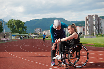 Image showing A Muslim woman wearing a burqa supports her friend with disability in a wheelchair as they train together on a marathon course.