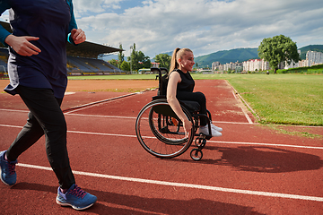 Image showing A Muslim woman in a burqa running together with a woman in a wheelchair on the marathon course, preparing for future competitions.