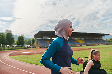 Image showing A Muslim woman in a burqa running together with a woman in a wheelchair on the marathon course, preparing for future competitions.