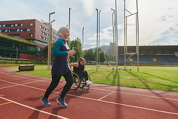 Image showing A Muslim woman in a burqa running together with a woman in a wheelchair on the marathon course, preparing for future competitions.