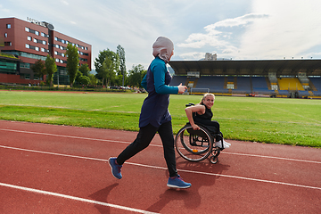 Image showing A Muslim woman in a burqa running together with a woman in a wheelchair on the marathon course, preparing for future competitions.